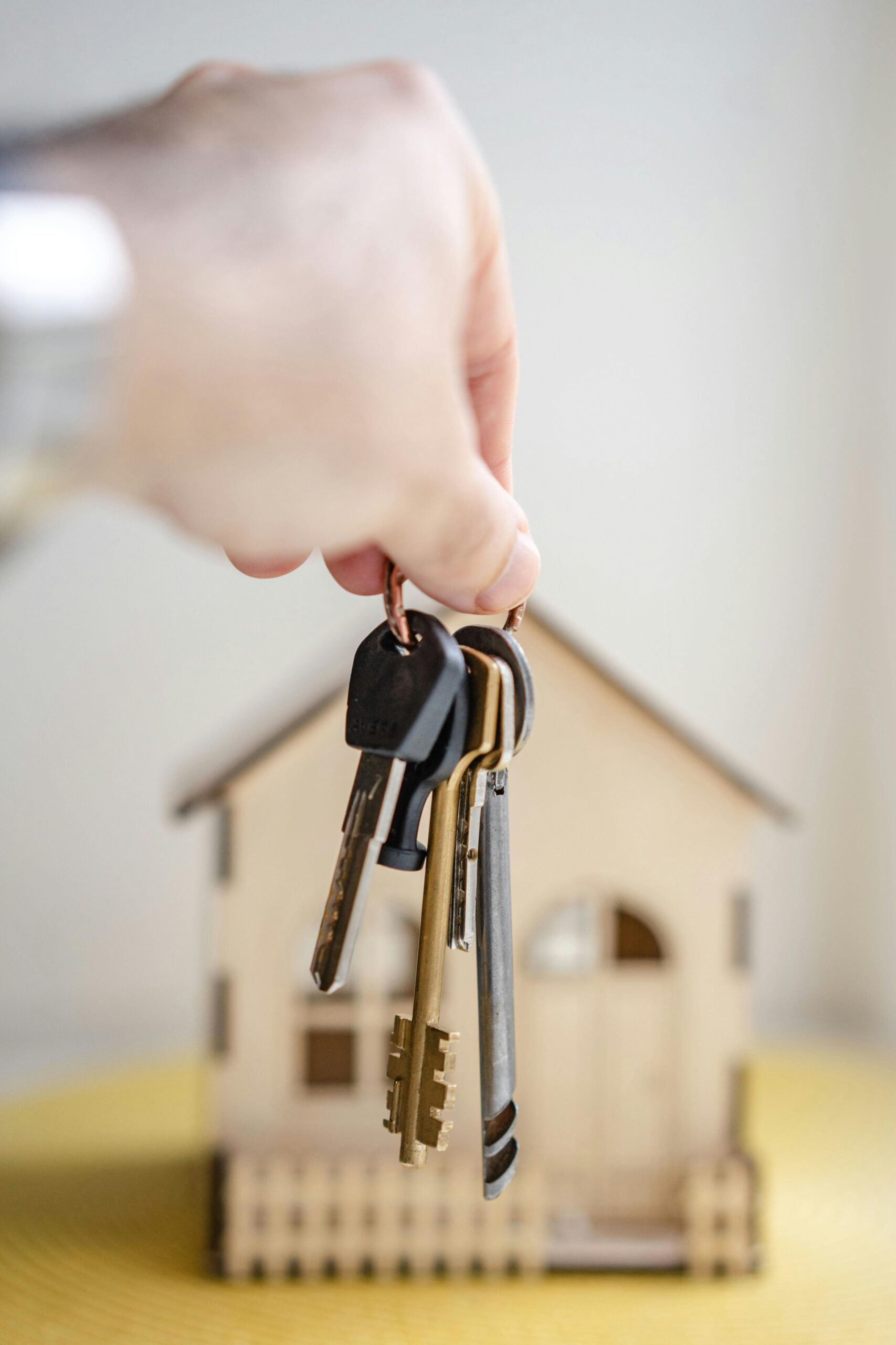hand holding a set of keys in front of a model of a house